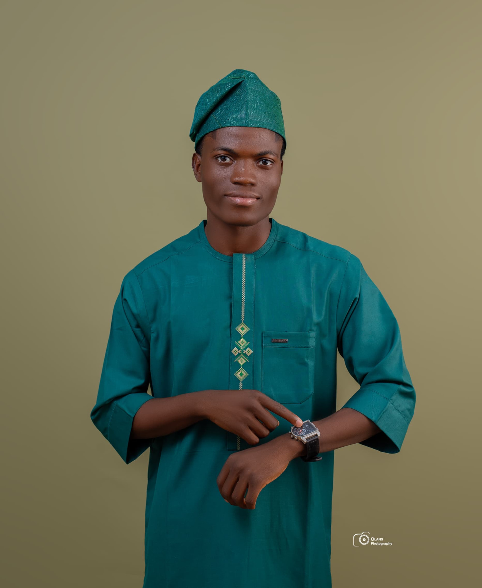 OGM in green traditional attire, pointing to the watch on his wrist